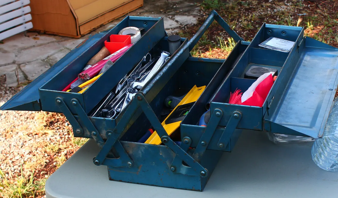 Une caisse à outils métallique bleue ouverte sur une table, remplie de clés, de tournevis et d'un niveau