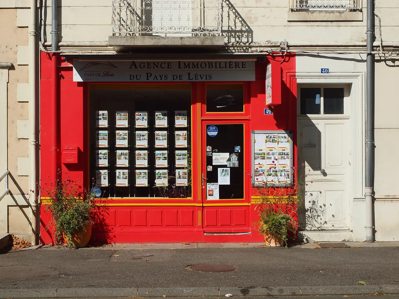 La vitrine rouge d'une agence immobilière de village, couverte d'annonces