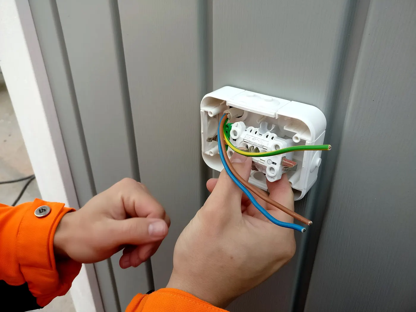 Deux mains raccordent les fils d'une prise murale