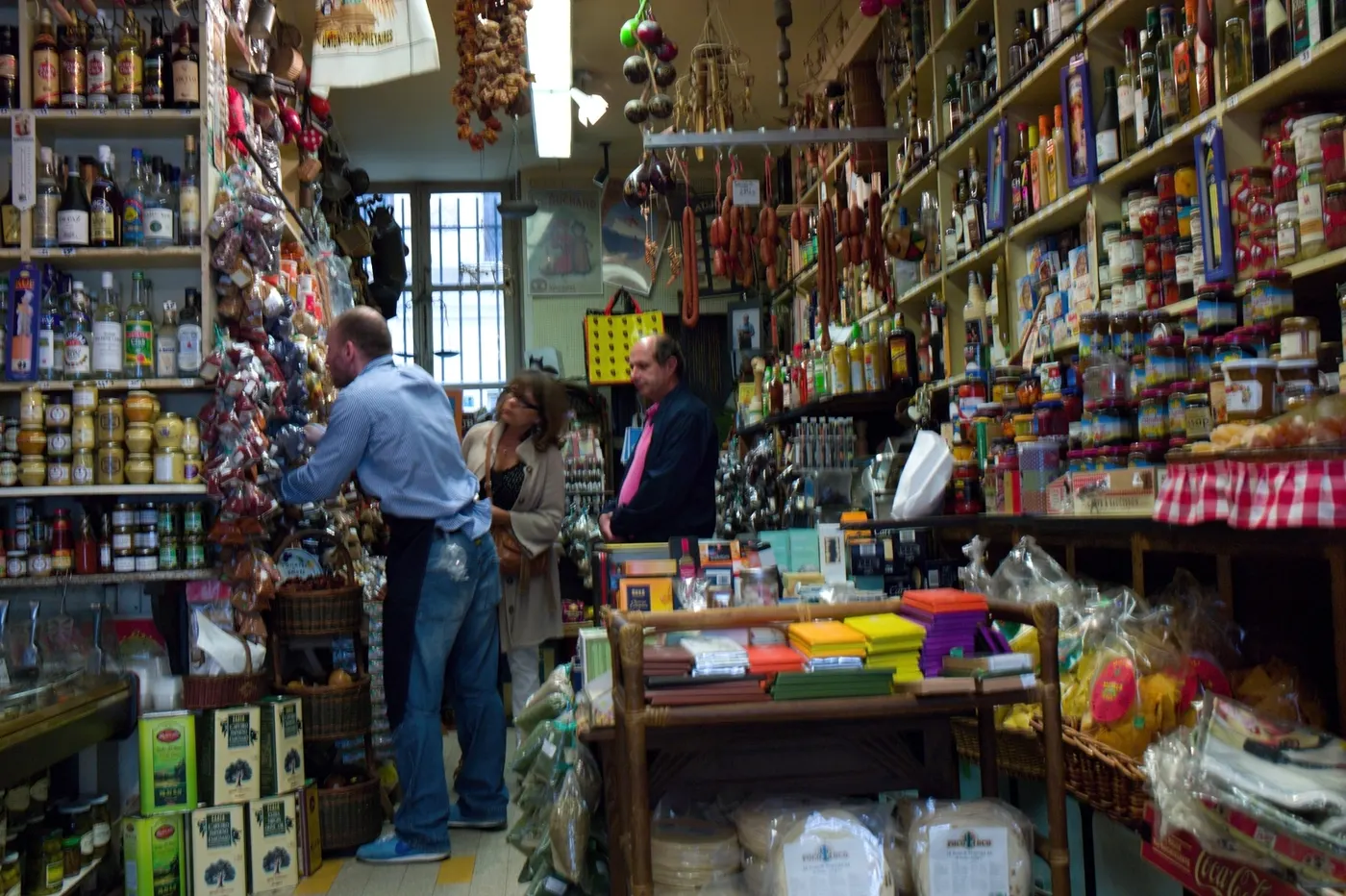 L'intérieur d'une épicerie fine aux rayons chargés jusqu'au plafond, trois personnes au comptoir